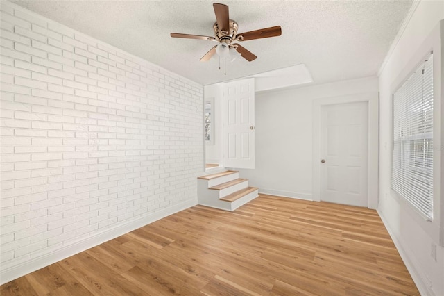 unfurnished room featuring brick wall, ceiling fan, a textured ceiling, and light wood finished floors