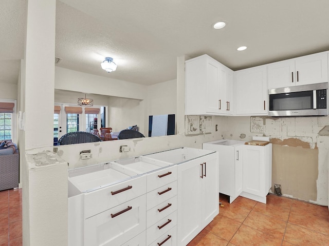 kitchen featuring stainless steel microwave, a sink, light countertops, backsplash, and light tile patterned flooring