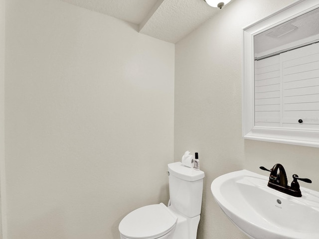 half bathroom with toilet, a textured ceiling, and a sink