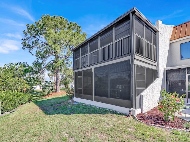 view of side of home with a sunroom, a standing seam roof, stucco siding, and a yard