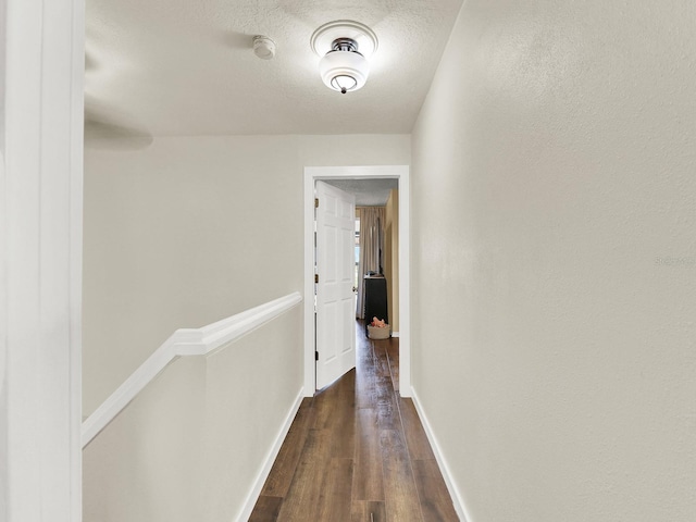 hallway featuring a textured ceiling, dark wood-style flooring, an upstairs landing, and baseboards