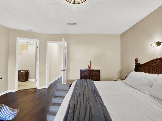 bedroom featuring baseboards, a textured ceiling, visible vents, and dark wood-style flooring