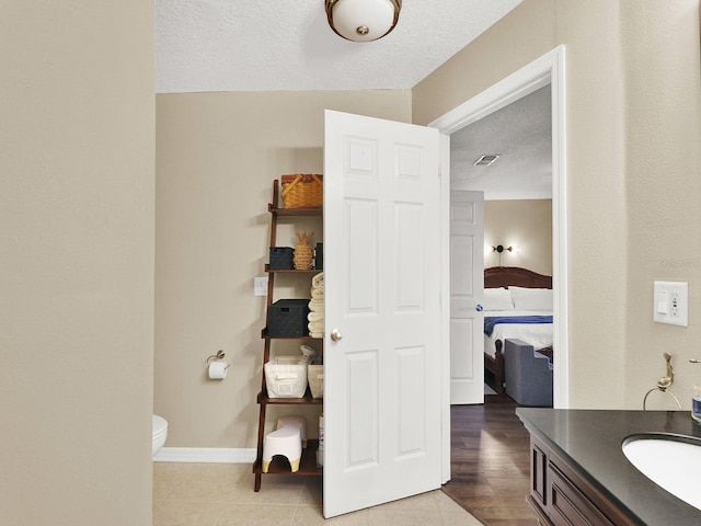 ensuite bathroom with a textured ceiling, toilet, vanity, visible vents, and baseboards