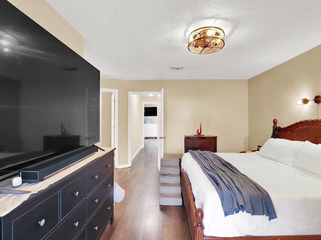 bedroom with a textured ceiling, dark wood-type flooring, visible vents, and baseboards