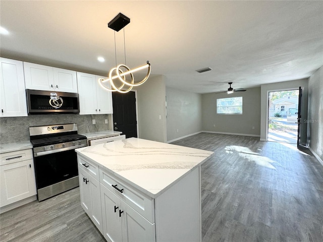 kitchen with a ceiling fan, stainless steel appliances, light wood-style floors, tasteful backsplash, and a center island