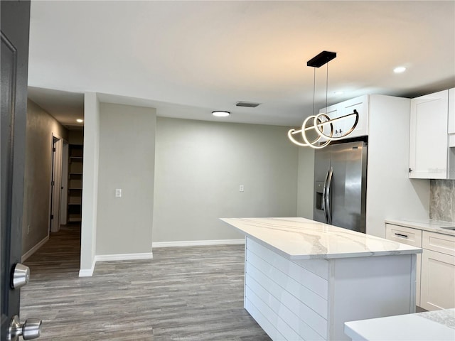 kitchen with light stone counters, visible vents, stainless steel refrigerator with ice dispenser, white cabinetry, and light wood-type flooring