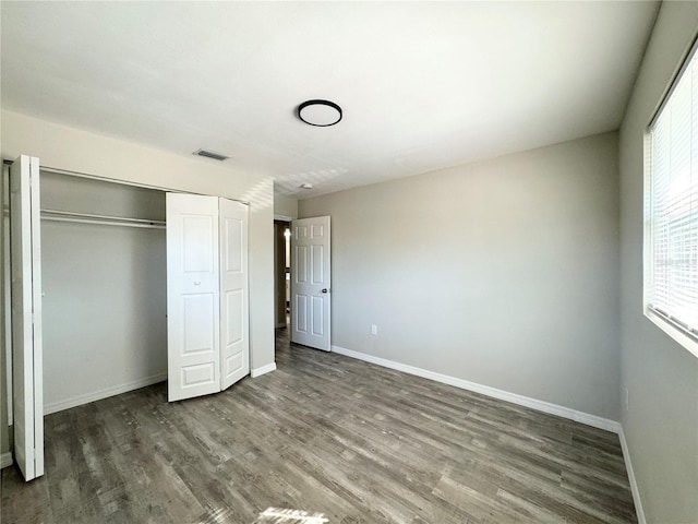 unfurnished bedroom with a closet, visible vents, baseboards, and wood finished floors