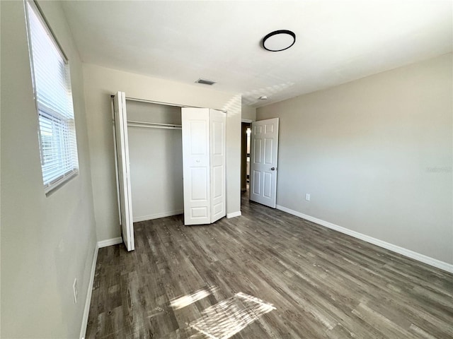 unfurnished bedroom with a closet, visible vents, baseboards, and dark wood-style flooring