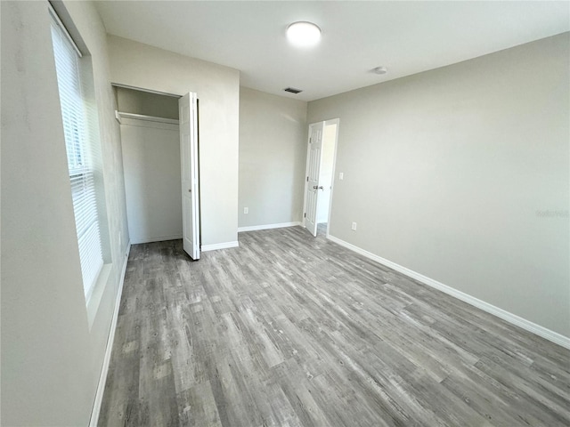 unfurnished bedroom featuring visible vents, wood finished floors, baseboards, and a closet