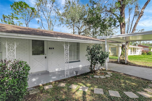 doorway to property with concrete driveway, a carport, and brick siding