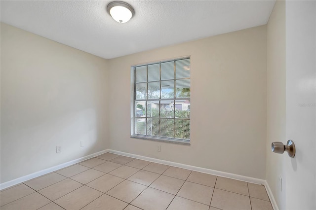 empty room with light tile patterned floors, baseboards, and a textured ceiling