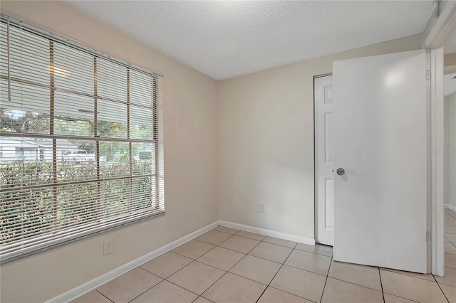 unfurnished room featuring light tile patterned floors, baseboards, and a textured ceiling