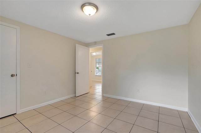 spare room with a textured ceiling, light tile patterned flooring, visible vents, and baseboards