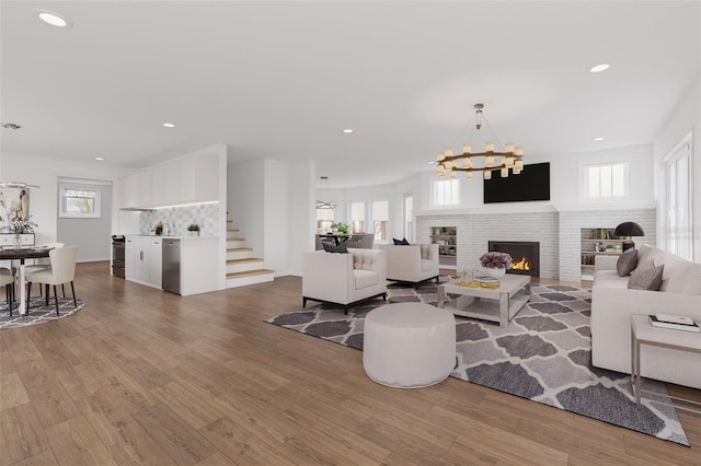 living area with recessed lighting, a warm lit fireplace, stairway, and wood finished floors