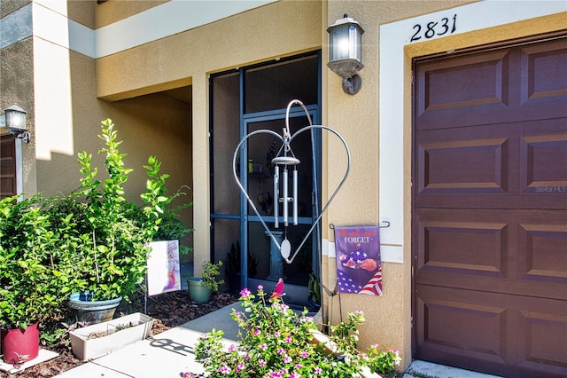 view of exterior entry with a garage and stucco siding