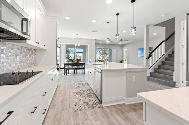 kitchen with stainless steel appliances, backsplash, a kitchen island with sink, white cabinets, and a sink