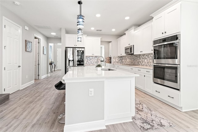 kitchen with white cabinets, decorative backsplash, appliances with stainless steel finishes, light countertops, and a sink