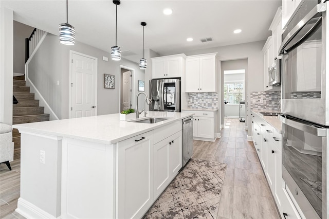 kitchen with stainless steel appliances, a sink, visible vents, white cabinets, and tasteful backsplash