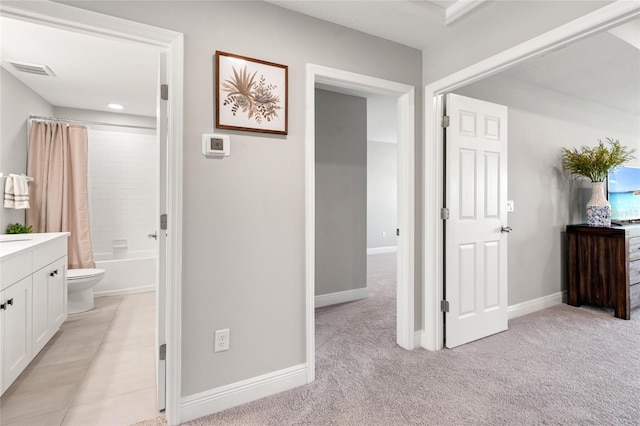 hall featuring baseboards, visible vents, and light colored carpet