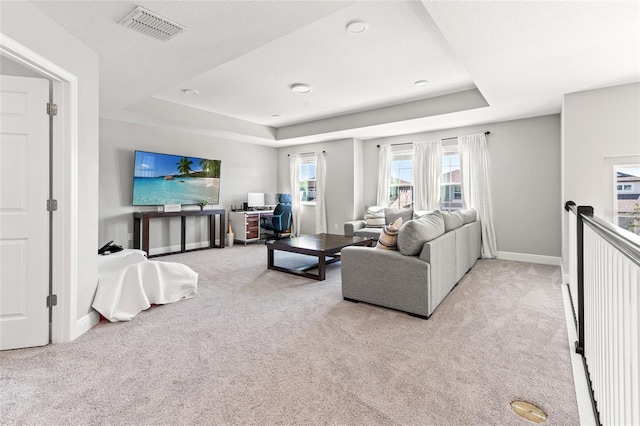 living room featuring a tray ceiling, carpet flooring, visible vents, and baseboards