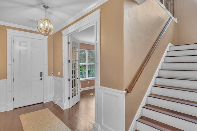 foyer with ornamental molding, dark wood-style flooring, a wainscoted wall, and stairway