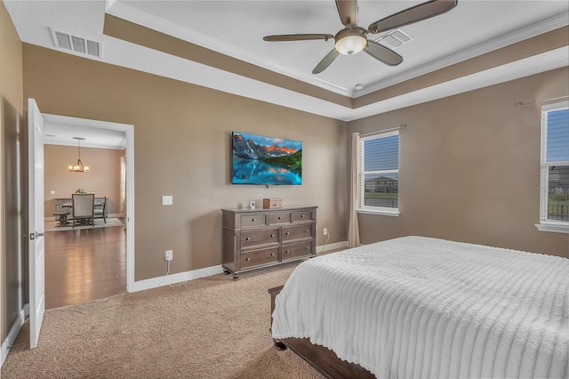 carpeted bedroom featuring baseboards, visible vents, a tray ceiling, and ceiling fan with notable chandelier