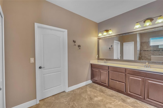 bathroom with a sink, a tile shower, baseboards, and double vanity