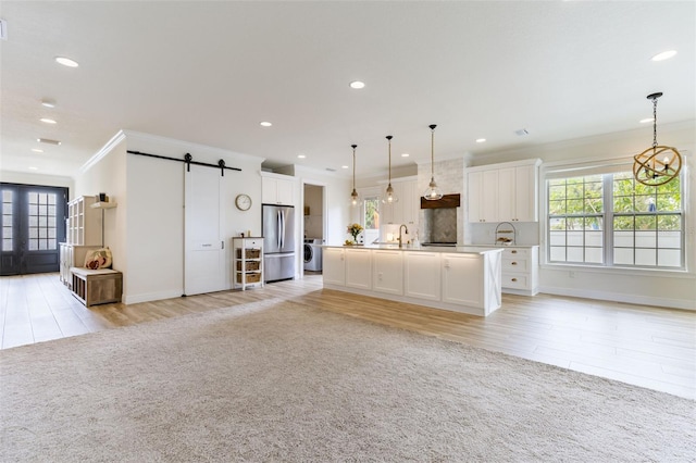 unfurnished living room with washer / dryer, a barn door, light colored carpet, ornamental molding, and recessed lighting