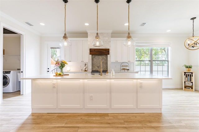 kitchen featuring washer / clothes dryer, light countertops, light wood-style floors, white cabinetry, and a large island with sink