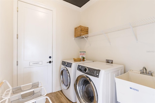 laundry room featuring crown molding, light wood-style flooring, a sink, laundry area, and independent washer and dryer