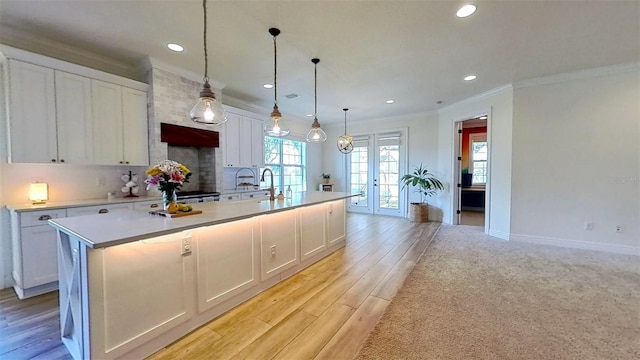 kitchen featuring white cabinetry, light countertops, french doors, a center island with sink, and crown molding