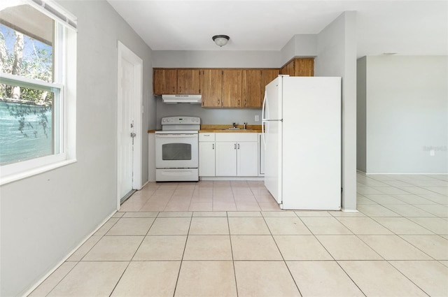 kitchen featuring light countertops, brown cabinetry, light tile patterned flooring, white appliances, and under cabinet range hood