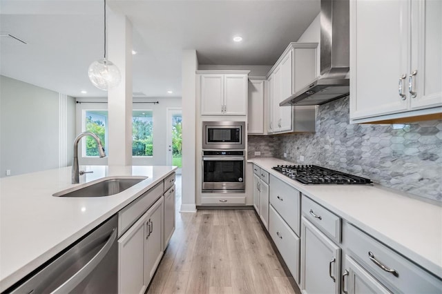 kitchen featuring a sink, appliances with stainless steel finishes, light countertops, and wall chimney range hood