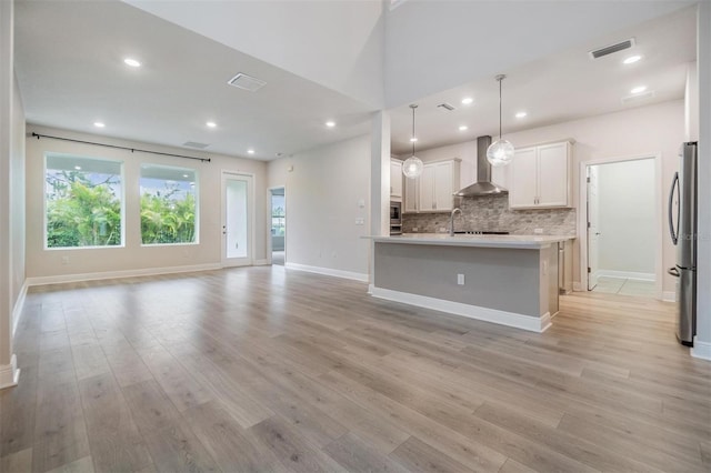 kitchen featuring visible vents, appliances with stainless steel finishes, wall chimney range hood, light wood-type flooring, and backsplash