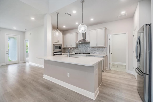 kitchen with a sink, light countertops, appliances with stainless steel finishes, wall chimney range hood, and tasteful backsplash