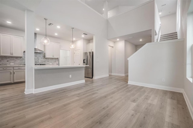 kitchen with open floor plan, wall chimney exhaust hood, light wood-style floors, and stainless steel fridge with ice dispenser