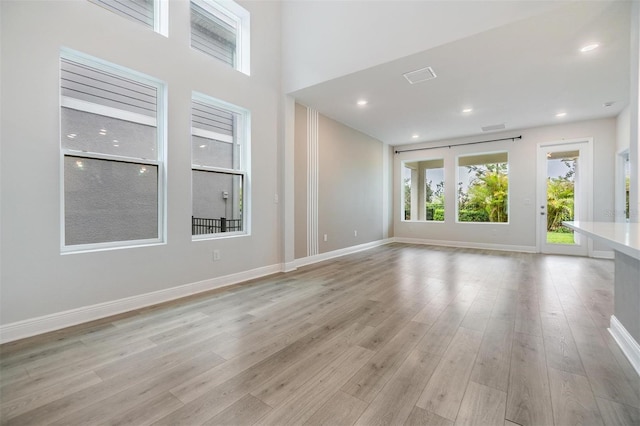 empty room with visible vents, baseboards, recessed lighting, a high ceiling, and light wood-style floors