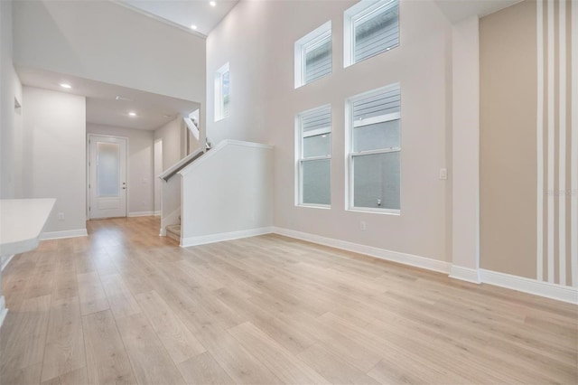 interior space with baseboards, recessed lighting, stairs, light wood-style floors, and a towering ceiling