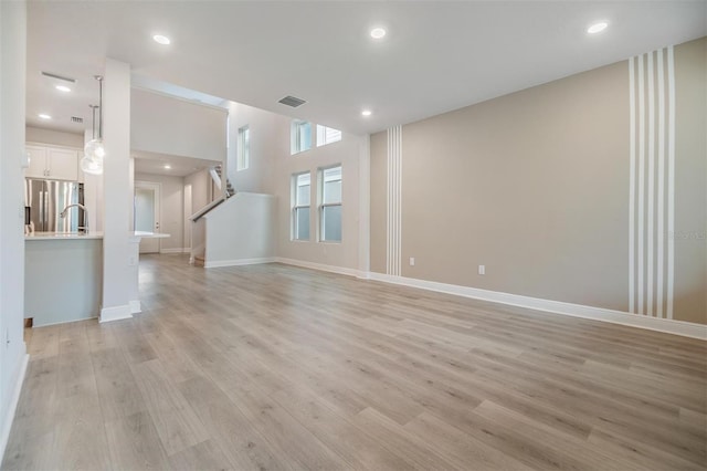 unfurnished living room with light wood finished floors, visible vents, recessed lighting, and baseboards