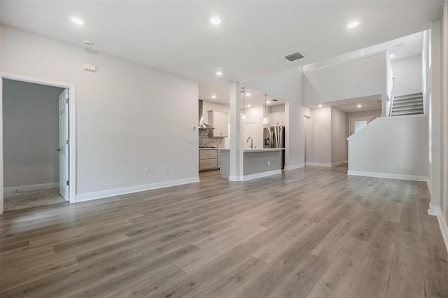 unfurnished living room featuring stairs, recessed lighting, light wood-style floors, and a sink