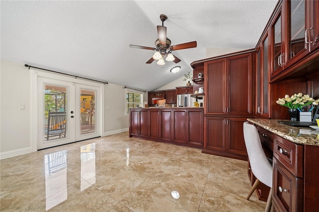 kitchen with reddish brown cabinets, french doors, lofted ceiling, glass insert cabinets, and a textured ceiling