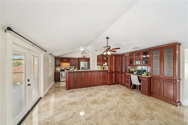 kitchen featuring a peninsula, vaulted ceiling, appliances with stainless steel finishes, reddish brown cabinets, and built in desk