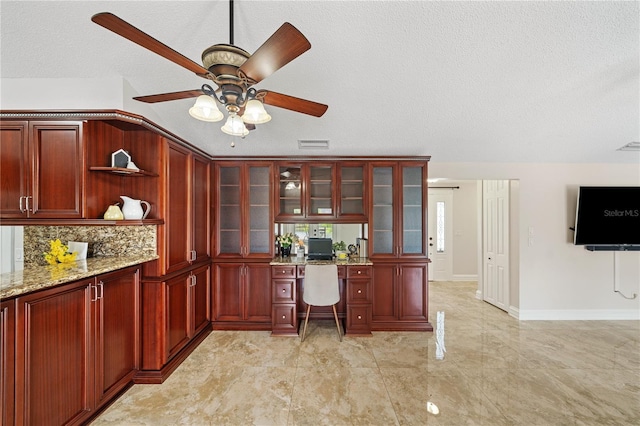 office space with a textured ceiling, ceiling fan, visible vents, baseboards, and built in study area