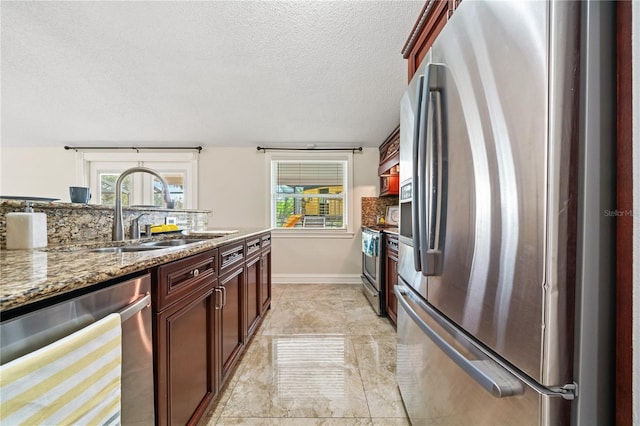 kitchen featuring appliances with stainless steel finishes, stone counters, a healthy amount of sunlight, and a sink