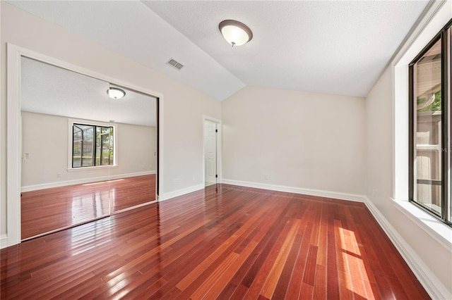 spare room featuring wood-type flooring, visible vents, vaulted ceiling, and baseboards