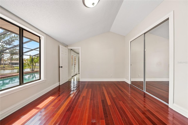 unfurnished bedroom featuring vaulted ceiling, a closet, wood-type flooring, and baseboards