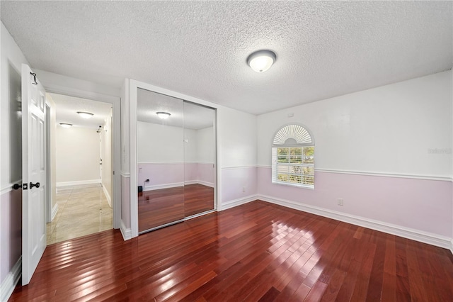 unfurnished bedroom with a textured ceiling, a closet, wood-type flooring, and baseboards