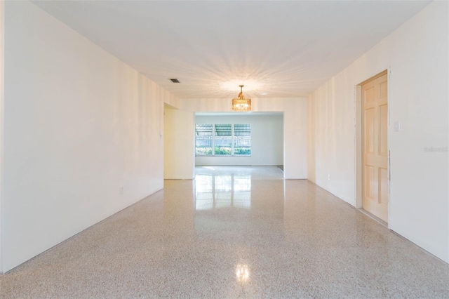 empty room featuring speckled floor, visible vents, and a notable chandelier