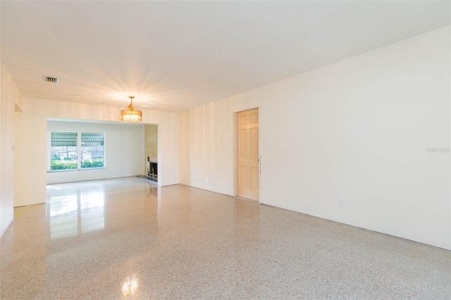 spare room featuring a large fireplace, visible vents, and speckled floor