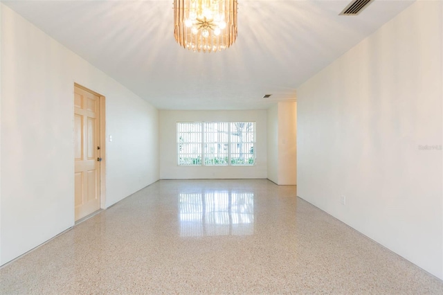 unfurnished room with visible vents, a notable chandelier, and speckled floor